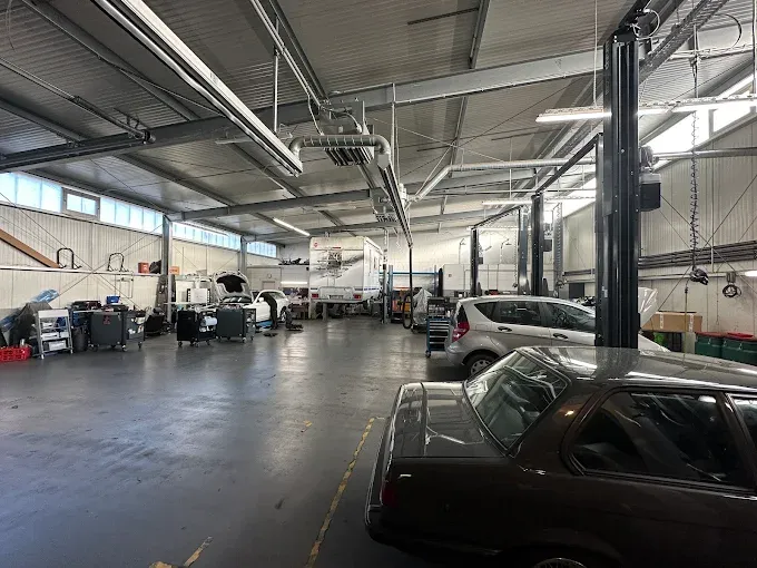 Blick in die Werkstatthalle: mehrere Fahrzeuge auf Hebebühnen und in Arbeitsbuchten, Werkzeugwagen an der Längswand